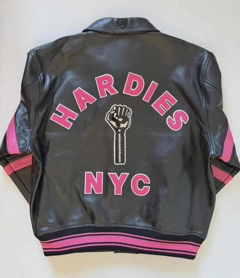 Puede incluir: Chaqueta de cuero negra con detalles rosas en las mangas y el bajo. La parte trasera presenta la palabra "HARDIES" en letras rosas sobre un pu&ntilde;o en blanco y negro, con "NYC" debajo.