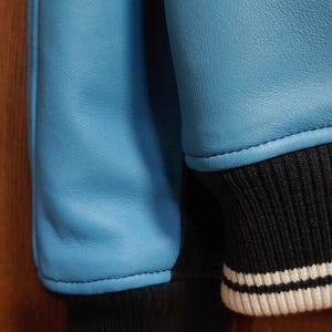 Peut inclure: Gros plan sur une veste bleu clair avec des poignets ray&eacute;s noirs et blancs. Les manches de la veste sont d'un bleu clair uni et lisse, avec un poignet en tricot c&ocirc;tel&eacute; ray&eacute; noir et blanc.