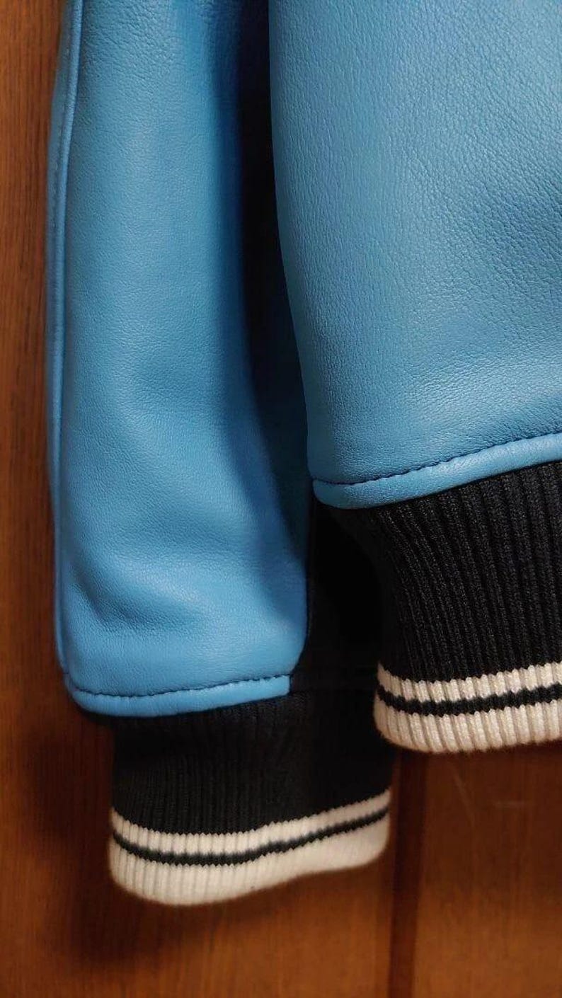 Peut inclure: Gros plan sur une veste bleu clair avec des poignets ray&eacute;s noirs et blancs. Les manches de la veste sont d'un bleu clair uni et lisse, avec un poignet en tricot c&ocirc;tel&eacute; ray&eacute; noir et blanc.