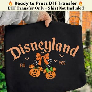 May include: A black DTF transfer featuring the orange text Disneyland, Est. 1955, and two pumpkin characters with mouse ears. One pumpkin has an orange bow, the other a green bow, connected by a spiderweb design with small bats surrounding them.