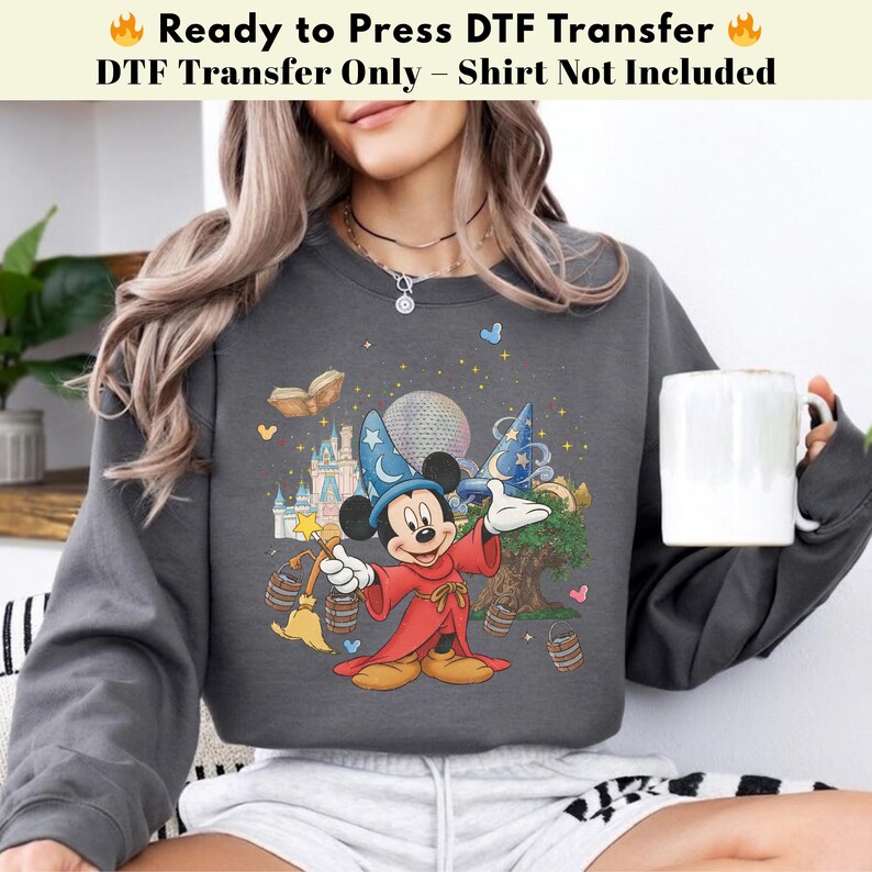 Pode incluir: Camisola cinza escuro com um gr&aacute;fico colorido do Mickey Mouse como um mago, com um castelo, um globo e outros elementos m&aacute;gicos. O texto na parte superior diz "Ready to Press DTF Transfer" e "DTF Transfer Only - Shirt Not Included."
