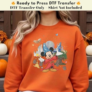 Pode incluir: Camisola laranja com uma transfer&ecirc;ncia DTF do Mickey Mouse como feiticeiro. O design inclui um castelo, um globo e outros elementos m&aacute;gicos. O texto na parte superior diz "Ready to Press DTF Transfer" e "DTF Transfer Only - Shirt Not Included."