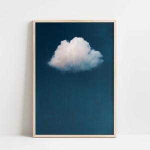May include: A framed print showing a single, fluffy white cloud set against a dark blue sky. The cloud is centrally positioned, offering a minimalist and calm feel. The frame is a light wood colour.