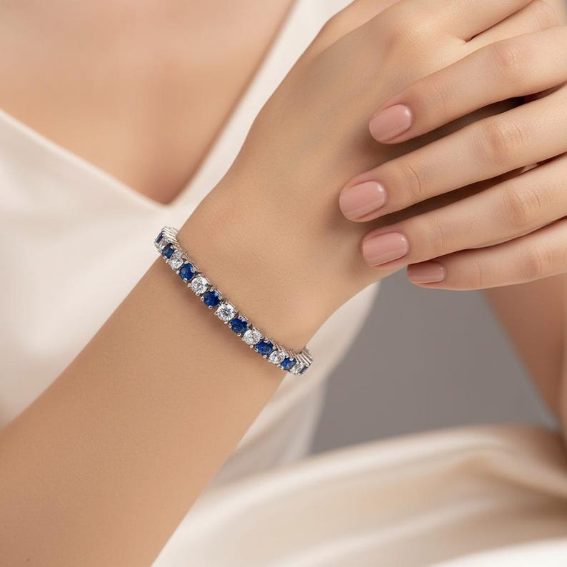 May include: A tennis bracelet with alternating round blue and clear gemstones. The bracelet is worn on a wrist, showcasing the sparkling stones. The bracelet is a piece of jewelry, likely made of silver or white gold.