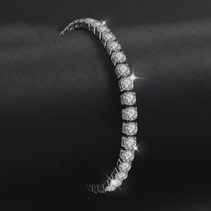 May include: A silver tennis bracelet with multiple round-cut, sparkling gemstones. The bracelet is curved, with the gemstones set closely together. The background is a dark, textured surface, creating a contrast with the bright bracelet.