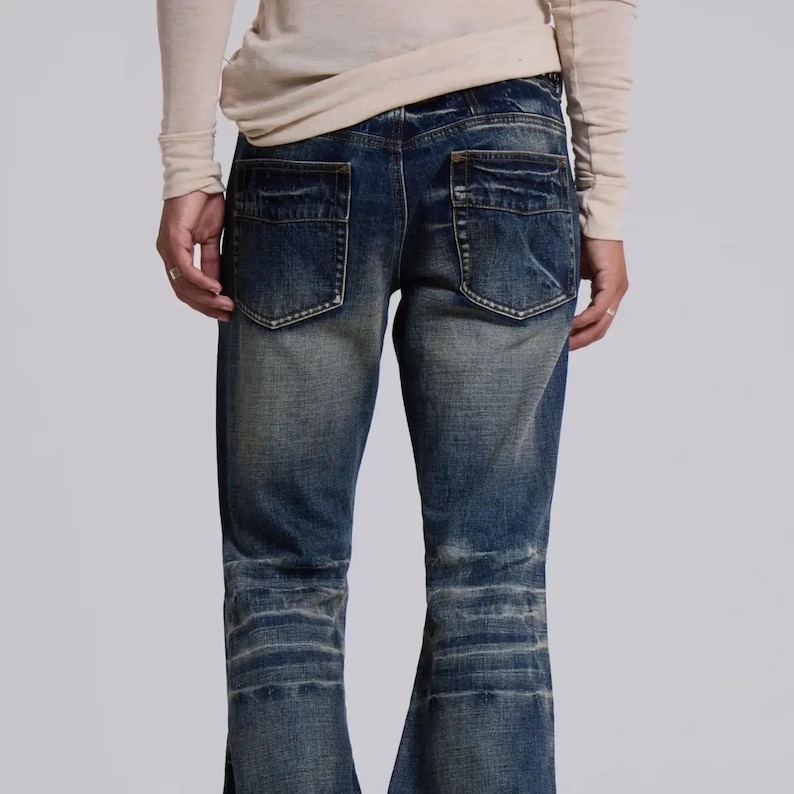 Op de afbeelding: Verbleekte blauwe denim jeans met een distressed look. De jeans heeft twee achterzakken en een uitlopende pijp. De denim heeft een versleten uiterlijk met lichtere plekken en subtiele vervaging.