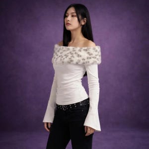 May include: White off-the-shoulder top with long sleeves and a faux fur leopard print collar. The top is paired with black jeans and a black belt. The sleeves flare out at the wrists. The background is a solid purple.