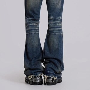 Op de afbeelding: Verbleekte blauwe denim jeans met distressed details. De jeans hebben een wijde beenopening en een versleten uiterlijk. De onderkant van de jeans is gerafeld. De jeans worden gecombineerd met zwarte schoenen met zilveren accenten.