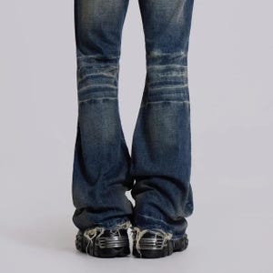 Op de afbeelding: Verbleekte blauwe spijkerbroek met distressed details op de knie&euml;n en gerafelde zomen. De jeans heeft een wijde, uitlopende pijp en wordt gecombineerd met zwarte plateauschoenen met metallic accenten.