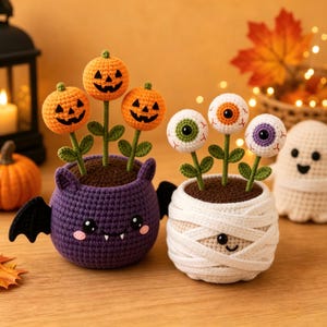 Pode incluir: Duas plantas em vaso de crochê com temas de Halloween. Um vaso roxo em forma de morcego contém três flores de abóbora laranja. O outro vaso branco enrolado como múmia contém três flores de globo ocular com íris verde, laranja e roxa.