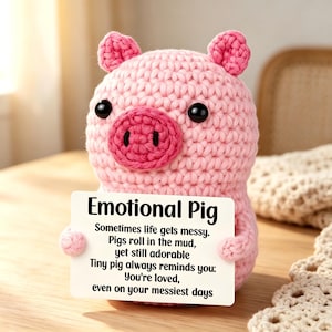 May include: A light pink crocheted pig figurine with black bead eyes and a darker pink snout. The pig holds a white rectangular card with the text: Emotional Pig, Sometimes life gets messy. Pigs roll in the mud, yet still adorable. Tiny pig always reminds you: You're loved, even on your messiest days.