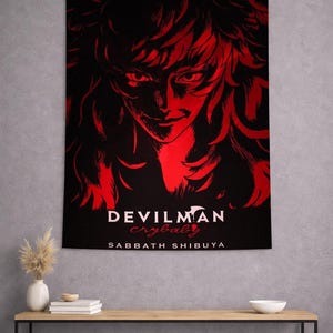 Könnte beinhalten: Schwarzes Wandtuch mit einer roten Illustration eines Gesichts mit langen Haaren. Der Text "DEVILMAN crybaby SABBATH SHIBUYA" ist unten in Weiß gedruckt. Es hängt an einer grauen Wand.