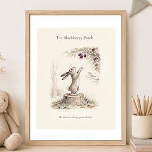 May include: A framed wall art print titled The Blackberry Patch featuring a watercolor illustration of a rabbit standing on a tree stump reaching for blackberries. The text below the illustration reads, The sweetest things grow slowly.
