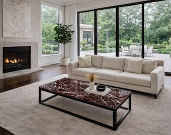 Puede incluir: Una mesa de centro rectangular con una superficie de mármol rojo intenso con vetas blancas y una estructura de metal negro. La mesa está colocada sobre una alfombra de color claro en una sala de estar, junto a un sofá beige y una chimenea.