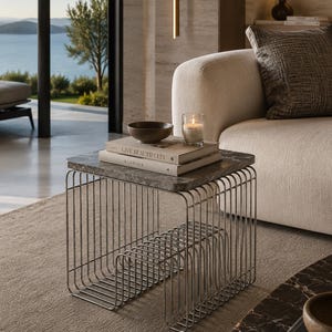 May include: A square side table with a dark gray marble top and a base constructed from thin, vertical silver metal rods. The table features a built-in storage rack at the bottom and holds two stacked books titled Live Beautifully and Kinfolk.