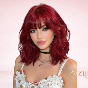 May include: A woman with red wavy hair and bangs. She is wearing a black choker and layered necklaces. Her top is white with a floral pattern. The image has the text "ZELYA Wigs" in the bottom right corner.