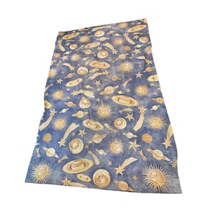 Peut inclure: Un textile rectangulaire orné d'un motif céleste sur fond bleu foncé. L'imprimé présente des illustrations dorées de soleils avec des visages, diverses planètes avec des anneaux, des étoiles et des comètes réparties sur toute la surface.