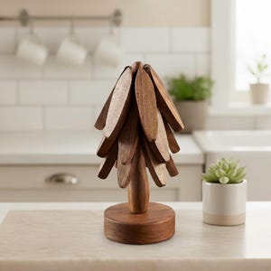 Op de afbeelding: Een houten decoratieve boom met een ronde basis en bladvormige stukken die zijn gerangschikt om op een boom te lijken. De boom is gemaakt van donkerbruin hout en staat op een lichtkleurig aanrecht. Hoogte ongeveer 20 cm.