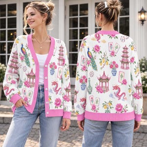 May include: A white long-sleeve button-down cardigan featuring a pink trim and a repeating pattern of colorful peacocks, pagodas, dragons, floral arrangements, and mahjong tiles. The knit garment has a V-neckline and ribbed cuffs and hem.