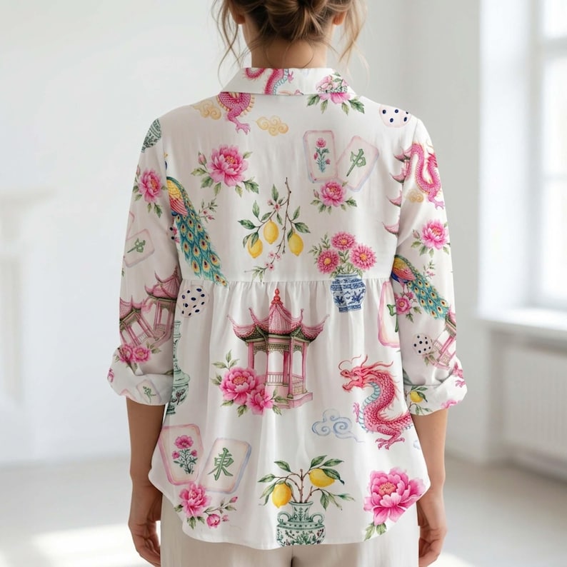 May include: A white long-sleeve button-down shirt featuring a colorful print of pink peonies, red dragons, pagodas, lemons, and mahjong tiles. The shirt has a collared neckline, a buttoned front, and long sleeves with rolled cuffs, showcasing a vibrant pattern.