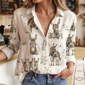 May include: A white long-sleeve button-down shirt featuring a repeating print of brown donkeys and various wildflowers. The shirt has a classic collar, a front button placket, and long sleeves with cuffs, showcasing a detailed animal and floral pattern.