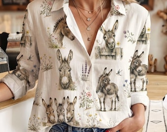 May include: A white long-sleeve button-down shirt featuring a repeating print of brown donkeys and various wildflowers. The shirt has a classic collar, a front button placket, and long sleeves with cuffs, showcasing a detailed animal and floral pattern.