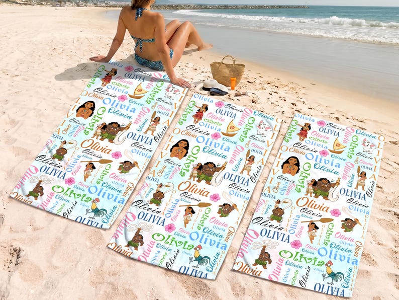 May include: Three rectangular beach towels featuring a repeating pattern of Moana characters, sailboats, and the name Olivia in various colorful fonts. The white towels are decorated with pink hibiscus flowers and brown wooden oars.