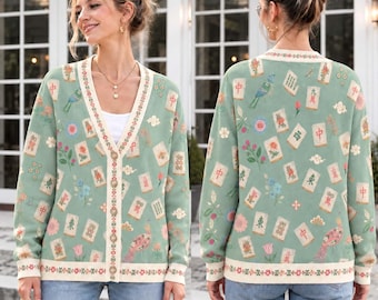 May include: A sage green V-neck cardigan featuring a repeating pattern of mahjong tiles, colorful floral motifs, and bird illustrations. The garment has a cream-colored button-down front placket with a decorative floral border and ribbed cuffs.