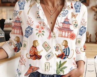 May include: A white long-sleeve button-down shirt featuring a colorful print of monkeys, pagodas, blue and white porcelain vases, cherry blossoms, and mahjong tiles. The shirt has a collar, a buttoned front, and cuffed sleeves.