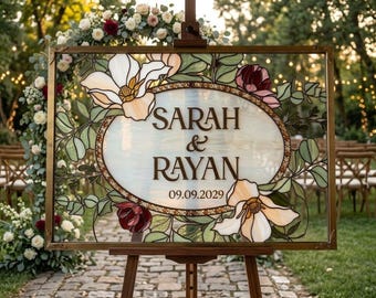 May include: A rectangular stained glass sign in a bronze frame featuring an oval center with the text SARAH & RAYAN and the date 09.09.2029. The design includes white and burgundy floral motifs with green leaves on a translucent background.