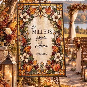 Könnte beinhalten: Ein rechteckiges Hochzeitsschild mit einem Rand im Buntglas-Stil, verziert mit Herbstblättern, weißen Blumen, roten Beeren und Kürbissen. Der mittlere Text lautet: the MILLERS, Olivia + Aaron, 12.12.2027. Auf einem Metallständer platziert.