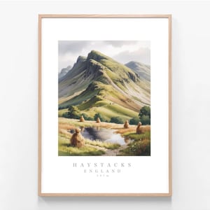 May include: A framed landscape print featuring a green mountain range under a cloudy sky, with a small pond and haystacks in the foreground. The text below the image reads HAYSTACKS ENGLAND 597m, presented in a light wood frame with a white mat border.