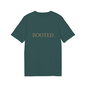 Könnte beinhalten: Ein dunkelgrünes T-Shirt mit dem Wort "ROOTED" in hellbrauner Schrift auf der Brust. Das Shirt hat kurze Ärmel und einen Rundhalsausschnitt. Der Text enthält die Buchstaben "ls" in einer kleineren Schriftart.