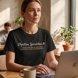 Pode incluir: Uma t-shirt preta de manga curta com texto em branco e dourado impresso no peito que diz Objection. Speculation. YOUR BRAIN IS WRITING WORST-CASE SCENARIOS. com um pequeno ícone branco de um martelo ao lado da palavra Speculation.