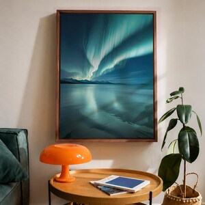 Pode incluir: Uma impressão de arte de parede emoldurada apresentando uma aurora boreal vibrante em tons de azul e turquesa sobre um corpo de água calmo e montanhas distantes. A obra está inserida numa moldura de madeira castanha escura e fina.