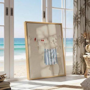 May include: A framed vertical wall art print featuring a light beige background with a clothesline illustration. The image displays a red bikini top and a blue and white striped towel hanging from wooden clothespins, casting soft shadows.