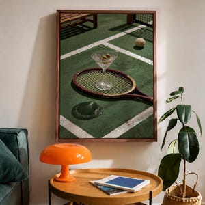 Könnte beinhalten: Ein gerahmter Kunstdruck zeigt eine Tennisszene mit einem Martini-Glas, Oliven und einem Tennisschläger. Ein Tennisball ist ebenfalls vorhanden. Das Kunstwerk ist vor einem grünen Hintergrund mit weißen Linien gehalten, was ein sportliches Thema suggeriert.