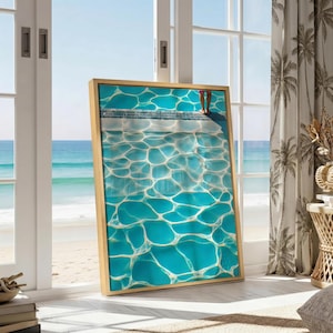 Puede incluir: Una pieza de arte mural rectangular enmarcada que presenta una vista desde arriba de una piscina con agua turquesa brillante y patrones de refracción de luz. Se ve el borde de la piscina con una rejilla oscura y unos pies al borde.