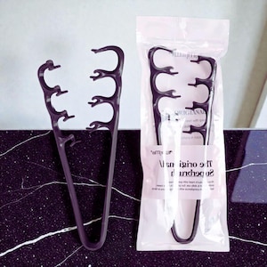 Puede incluir: Dos pinzas negras para espaguetis, una suelta y otra en un paquete de plástico transparente. Las pinzas tienen un diseño único con múltiples púas curvas para agarrar la pasta. El paquete tiene texto parcialmente visible.