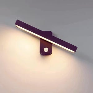 Pode incluir: Uma moderna luminária LED de parede. A luminária é marrom escuro com uma barra de luz retangular e giratória. A barra de luz emite uma luz branca brilhante. Um pequeno botão redondo está na base.