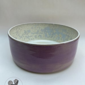 May include: A handmade ceramic bowl with a wide, shallow design. The exterior is a deep purple, while the interior features a speckled, light-coloured glaze. The bowl is from Rustic Hands Pottery.