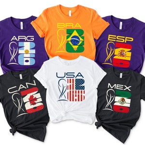 May include: A set of three ceramic mugs with a speckled, cream-colored glaze. Each mug features a different hand-painted design: a blue and green leaf, a yellow flower, and a red berry. The mugs have a simple, modern design.