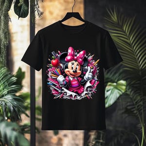 May include: Black t-shirt featuring a colorful graphic of Minnie Mouse in a pink dress and bow, surrounded by pencils, an apple, and hearts. The design has a cartoon style, perfect for Disney fans.