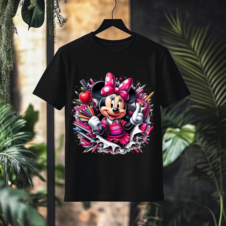 May include: Black t-shirt featuring a colorful graphic of Minnie Mouse in a pink dress and bow, surrounded by pencils, an apple, and hearts. The design has a cartoon style, perfect for Disney fans.