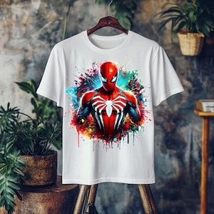 May include: White t-shirt featuring a vibrant graphic of Spider-Man. The superhero is depicted in his classic red and blue suit, with a white spider emblem on the chest. The design includes colorful paint splatter effects, creating a dynamic and eye-catching look.