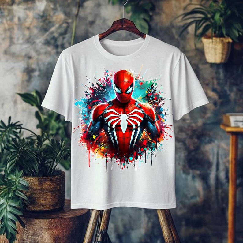 May include: White t-shirt featuring a vibrant graphic of Spider-Man. The superhero is depicted in his classic red and blue suit, with a white spider emblem on the chest. The design includes colorful paint splatter effects, creating a dynamic and eye-catching look.