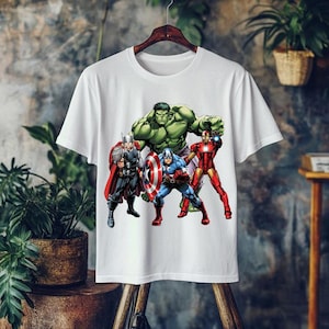 May include: White t-shirt featuring a graphic of the Avengers: Thor, Hulk, Captain America, and Iron Man. The superheroes are in action poses, with vibrant colors and detailed illustrations. The shirt is hanging on a wooden hanger.