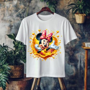 May include: White t-shirt featuring a colorful graphic of Minnie Mouse. Minnie is wearing a pink bow with white polka dots and a yellow dress. The graphic has a heart-shaped design with yellow and orange accents.