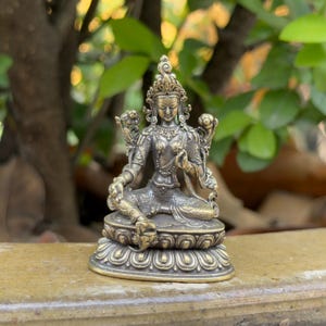 May include: A detailed bronze statue of a seated deity, adorned with intricate jewelry and a detailed headdress. The figure is seated on a lotus flower base, with a serene expression. The statue is approximately 4 inches tall.