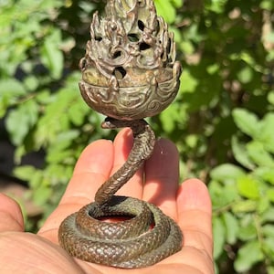 May include: A bronze-toned metal incense burner featuring a coiled snake base that supports a textured, flame-shaped upper vessel with openwork detailing. The object has a dark, weathered patina and a detailed scale pattern on the snake's body.